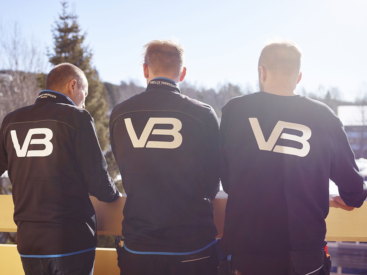 Tre VB Rørleggere med logo på baksiden av jakkene sine
